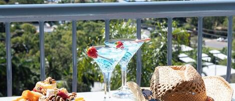 A balcony with a view of the sea, a plate of fruit, a cocktail, and a straw hat.