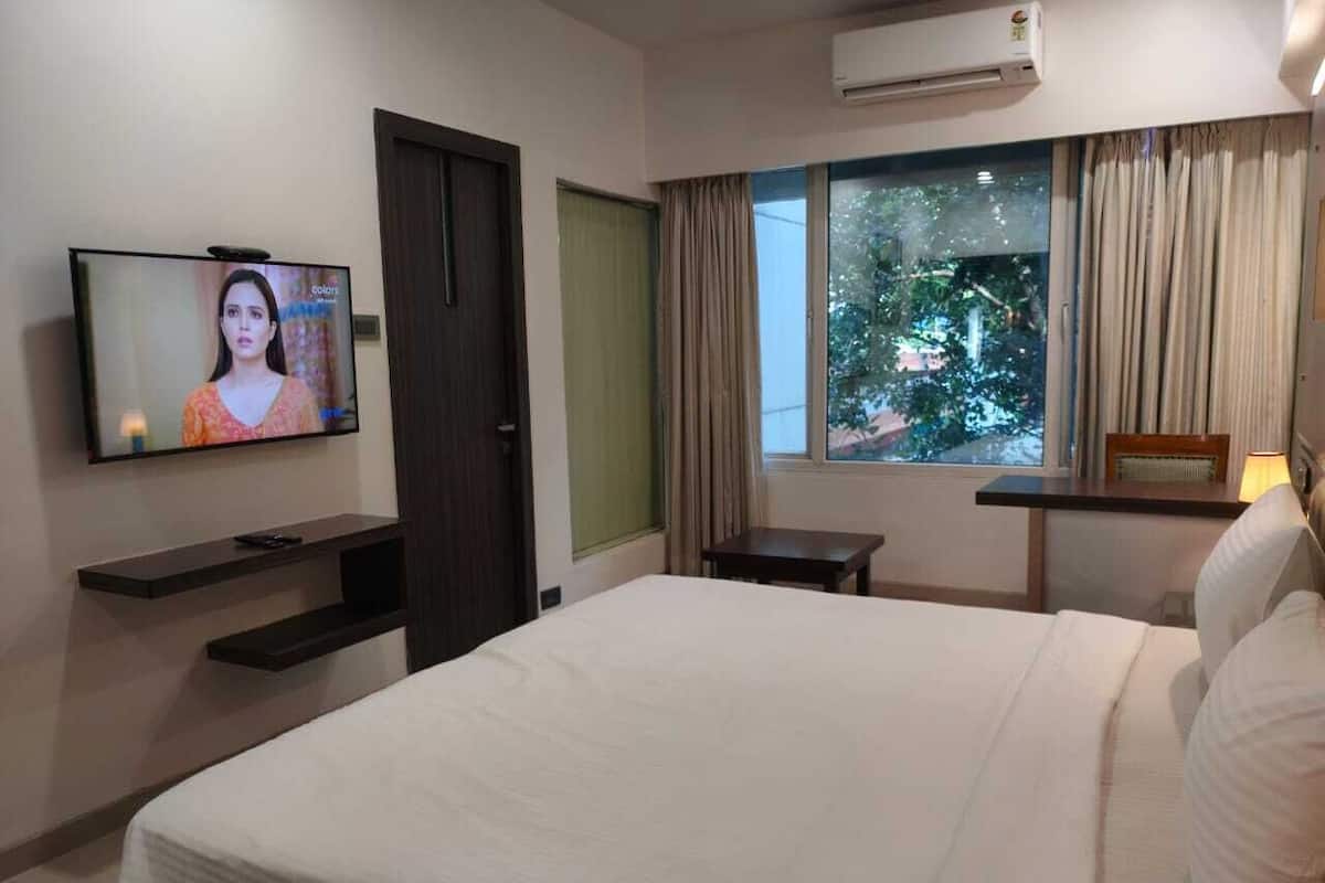 Habitación de hotel con cama, televisión, ventana con cortinas y aire acondicionado instalado en la pared.