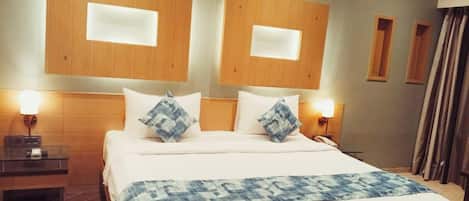 A hotel room with a large bed, two bedside tables, a headboard with built-in lighting, and a window with curtains.