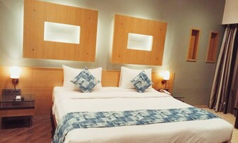 Habitación de hotel con una cama grande, dos mesitas de noche, cabecera con iluminación integrada y una ventana con cortinas.