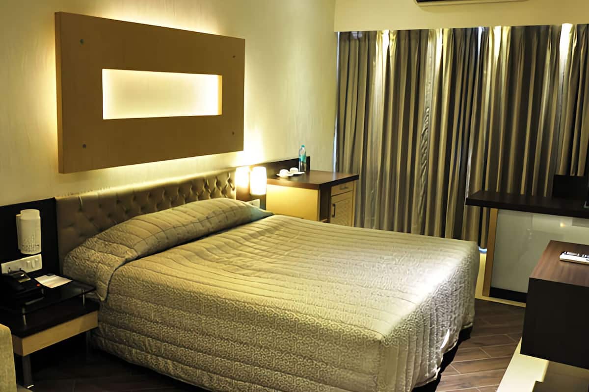 Una habitación de hotel con cama, mesita de noche, lámpara y vista a cortinas.