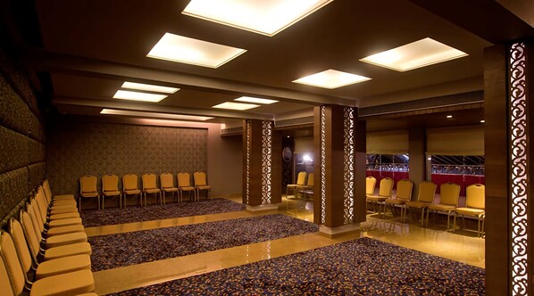 Un salón de conferencias con filas de sillas, una alfombra estampada e iluminación en el techo.