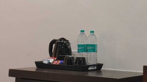 A framed artwork depicting architectural structures, a coffee maker, and two water bottles on a table.