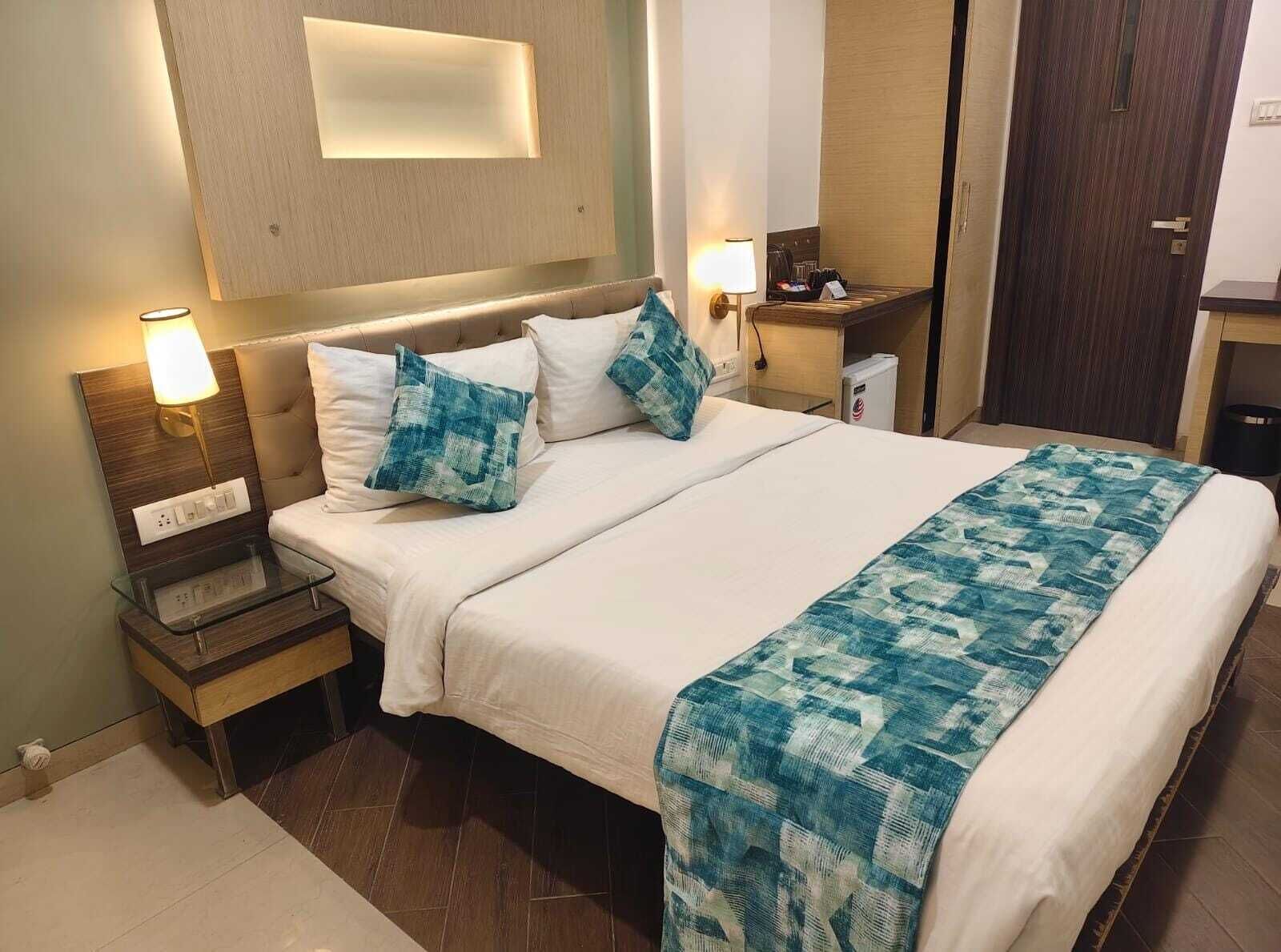 Una habitación de hotel con cama, lámparas de noche, una mesita de noche, una pequeña mesa y una puerta.