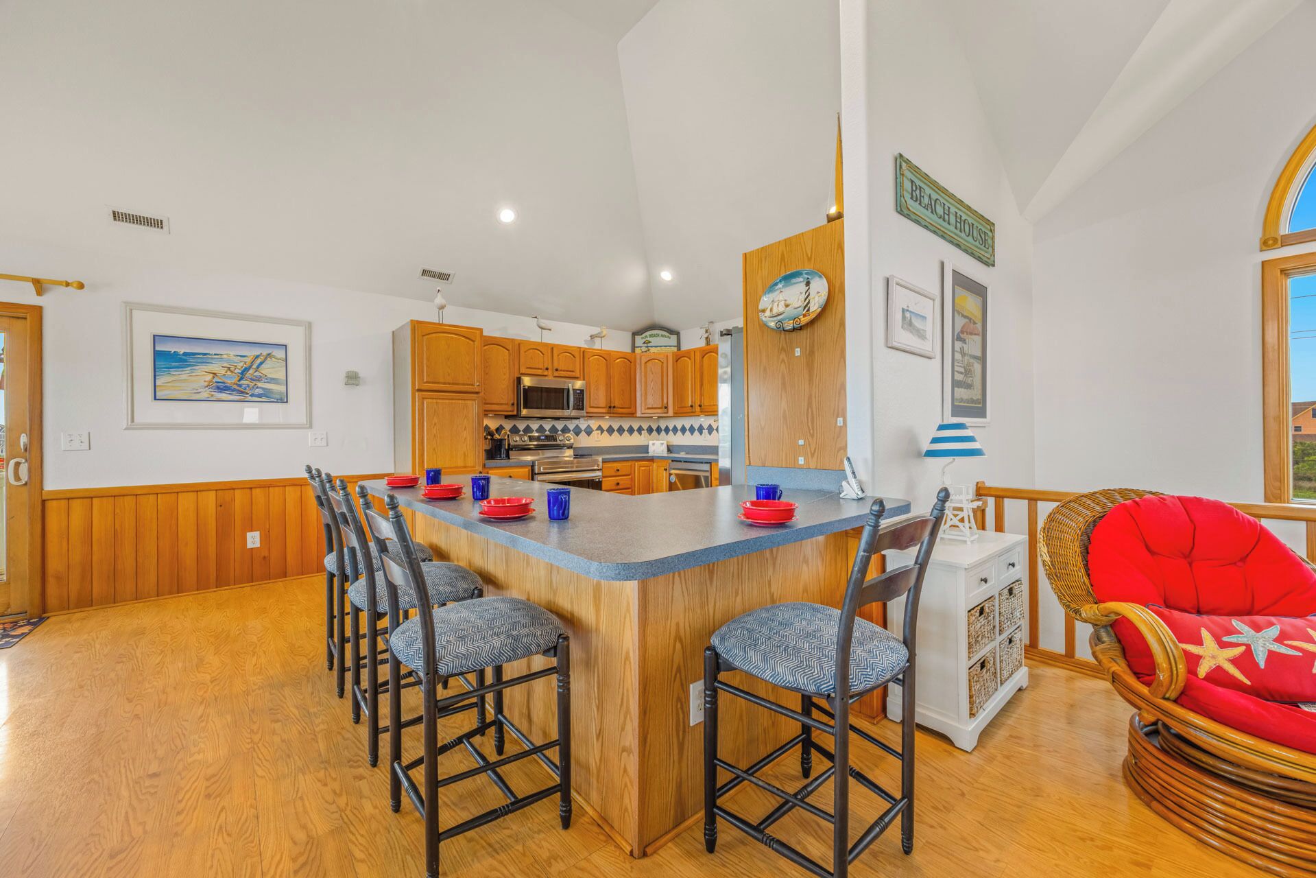 A spacious kitchen with wooden cabinets, a central island with bar stools, and a dining area with wicker furniture.