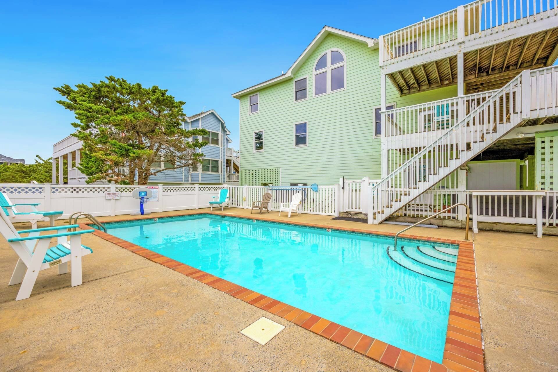 Piscina com espreguiçadeiras, um deck de madeira e um edifício de dois andares com varanda.