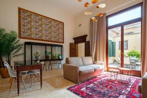 Un saló amb un sofà, una taula de centre, una taula de dinar amb cadires, una finestra gran amb cortines i una catifa colorida.