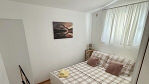 A bedroom with a bed, a painting, a window with curtains, and a bedside table with a lamp. - Apartment Didovi Dvori 2 With Jacuzzi (Razanac)