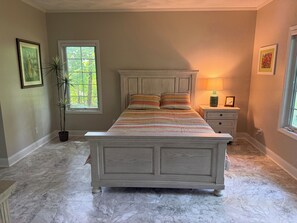 A bedroom with a bed, a nightstand, a lamp, a potted plant, and a window.