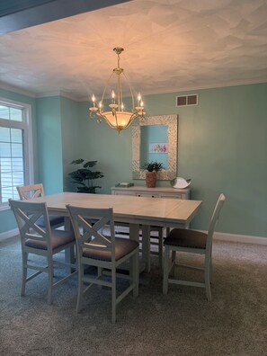 A dining room with a chandelier, a dining table, chairs, a potted plant, and a mirror on the wall.