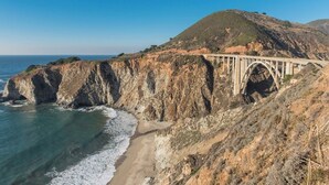 A coastal bridge with a clear view of the ocean and a hilly landscape. - 4082 Sea Sights - Ocean Views from Every Room (Carmel Highlands)