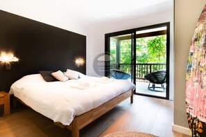 Une chambre à coucher avec un lit, des lampes de chevet, une vue sur l’extérieur grâce à une porte coulissante, et une chaise à l’extérieur.