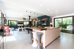 Eine moderne Küche mit Kochinsel, Barhocker und Essbereich mit einer Couch und Stühlen.