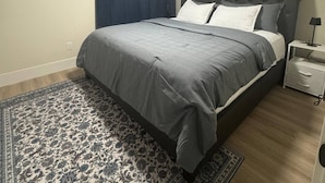 Un dormitorio con cama, mesita de noche, timón de barco en la pared, alfombra estampada y luz de techo.