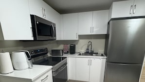 Una cocina moderna con armarios blancos, electrodomésticos de acero inoxidable, microondas, tostadora, cafetera y refrigerador.