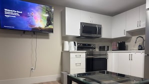 Una cocina moderna con armarios blancos, microondas, horno y una mesa con cubierta de vidrio.