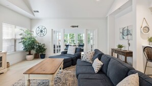 Ein geräumiges Wohnzimmer mit einem dunkelgrauen Sofa, einem Holztisch und einem großen Fenster mit Jalousien.