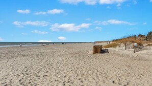 Ein weiter Sandstrand mit Fußspuren, einer Holzkonstruktion und einem klaren Himmel.