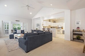 A spacious living area with a dark gray sofa, a wooden coffee table, and a patterned rug. There is a kitchen visible in the background with white cabinets and a microwave. - Shipyard Golf Master - Spacious 3 bedroom Beach, Pool, Tennis & Pickleball ! (Hilton Head Island)