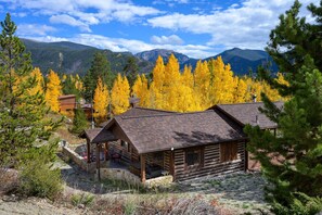 A log cabin with a porch, surrounded by autumn trees and mountains in the background. - Haskell Cabin 2 Bedroom Cabin (Grand Lake)