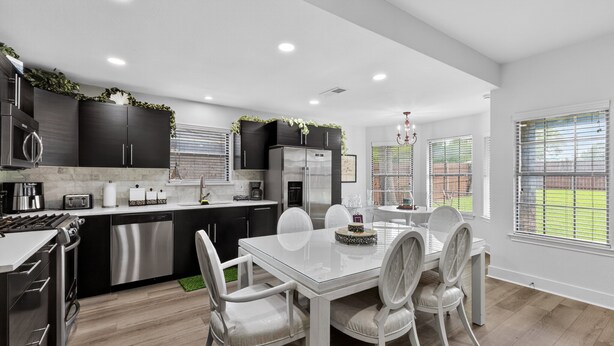 A modern kitchen with dark cabinetry, stainless steel appliances, and a dining area with a white table and chairs. - Central Frisco Family Getaway 3 Bedroom Home (Frisco)
