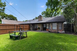 Une maison avec une façade en briques, une cheminée, une terrasse en bois et une cour gazonnée.