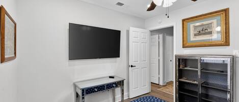 A bedroom with a ceiling fan, a TV mounted on the wall, a bed with a patterned bedspread, a white door, and a bookshelf.