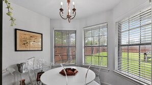 A dining area with a round table, chairs, a chandelier, and large windows with blinds. - Central Frisco Family Getaway 3 Bedroom Home (Frisco)