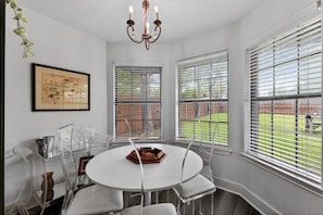 A dining area with a round table, chairs, a chandelier, and large windows with blinds. - Central Frisco Family Getaway 3 Bedroom Home (Frisco)