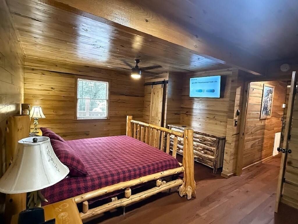 A wooden cabin room with a bed, a lamp, a ceiling fan, and a mounted television.