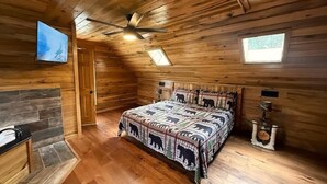 Un dormitorio tipo cabaña de madera con techo de madera, una cama con colcha temática de oso, chimenea y una pared de acento de piedra.