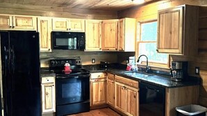 Una cocina con armarios de madera, un refrigerador negro, un microondas, una estufa y una cafetera.