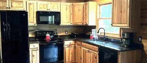 Una cocina con armarios de madera, un refrigerador negro, un microondas, una estufa y una cafetera.