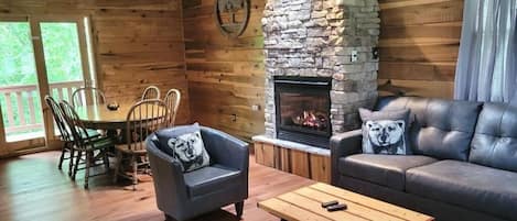 A wooden cabin interior with a stone fireplace, a dining table with chairs, a sofa, and a coffee table.