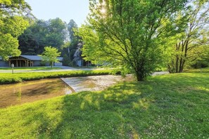 A grassy area with a small water feature, trees, and a building with a covered porch. - Mountain Stream 4 Bedroom Chalet (Pigeon Forge)
