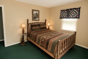 Un dormitorio con una cama de madera, dos lámparas de noche, un cuadro enmarcado en la pared y una ventana con cortina a cuadros.