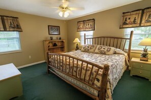 Une chambre à coucher avec un lit en bois, un bureau, une chaise, un ventilateur de plafond et une fenêtre avec des stores.
