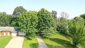 Ein Wohngebiet mit einer gepflasterten Auffahrt, die zu einem Haus führt, umgeben von üppigen Grünbäumen und einem kleinen Bach.