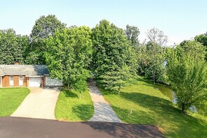 A residential area with a paved driveway leading to a house, surrounded by lush green trees and a small stream. - Mountain Stream 4 Bedroom Chalet (Pigeon Forge)