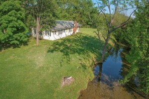 Une maison avec un toit en pente, entourée d’une cour verdoyante et d’un petit plan d’eau.