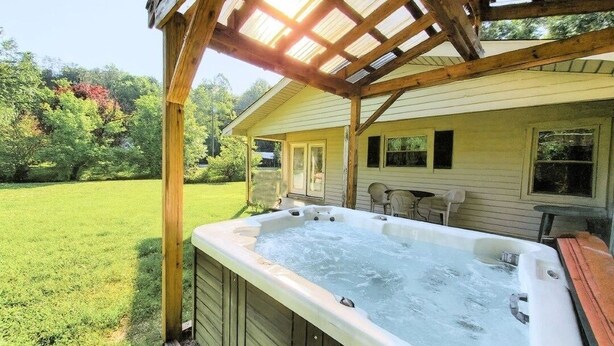 Ein Whirlpool unter einer Holzpergola, im Hintergrund ein Haus.