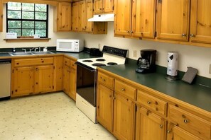 A kitchen with wooden cabinets, a stove, a microwave, and a coffee maker. - Smoky Mountain Memories 2 Bedroom Cabin (Pigeon Forge)