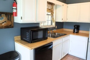 Cocina compacta con armarios blancos, microondas negro, cafetera y lavavajillas.