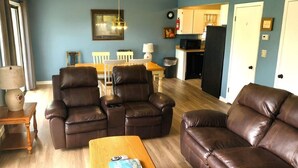 A living room with two brown leather sofas, a wooden coffee table, and a dining area with a white table and chairs. - Hillbilly Hilton 2 Bedroom Chalet (Pigeon Forge)