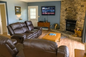A living room with a stone fireplace, leather sofas, a television, and a small table. - Hillbilly Hilton 2 Bedroom Chalet (Pigeon Forge)