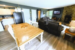 Ein Wohnzimmer mit Esstisch aus Holz, einer schwarzen Ledersofa, einem Kamin aus Stein und einem an der Wand befestigten Fernseher.