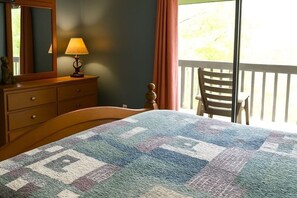 Un dormitorio con cama, cómoda, lámpara, silla y un balcón con barandilla.