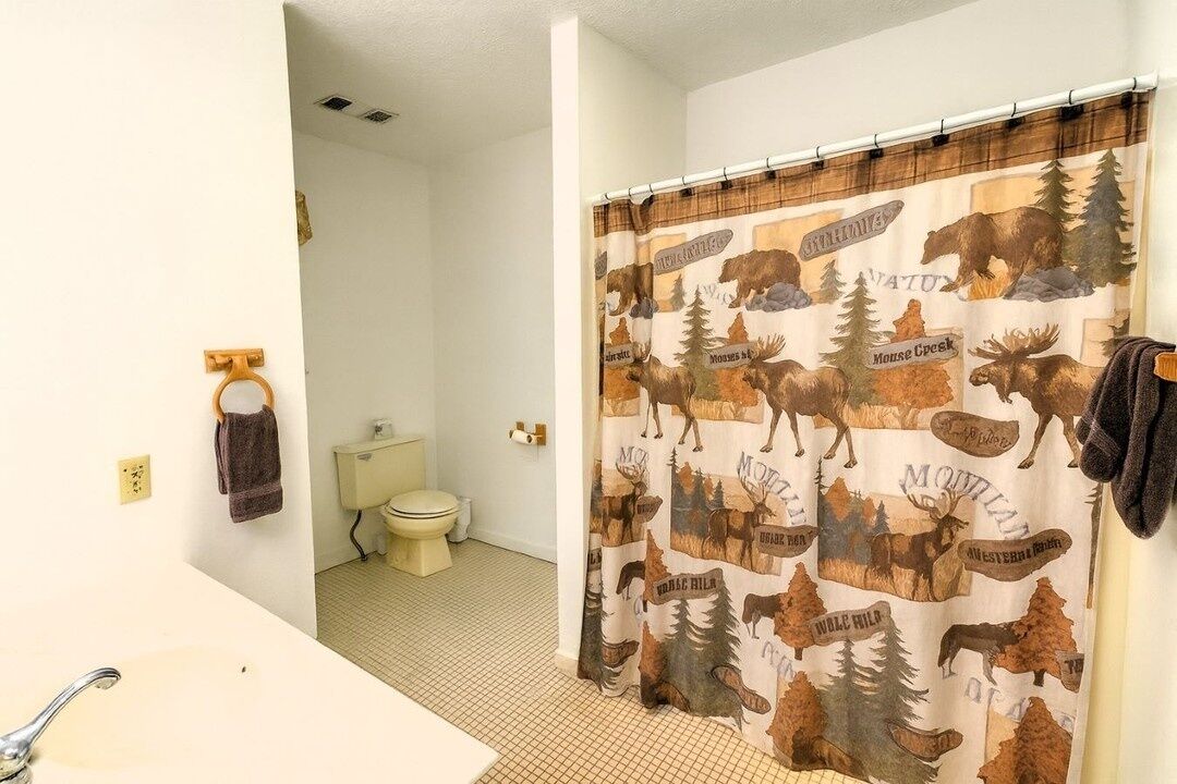 Un baño con cortina de ducha con estampados de animales, un inodoro y un lavabo con un perchero para toallas.