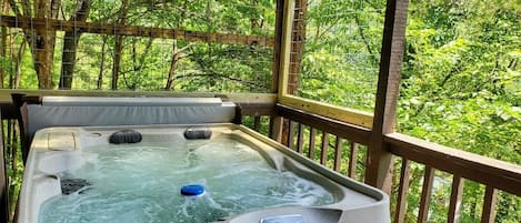 A hot tub on a wooden deck with a view of a forest.