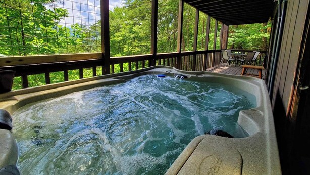 A hot tub with a wooden deck and a view of a forest. - Hillbilly Hilton 2 Bedroom Chalet (Pigeon Forge)